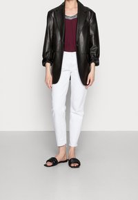 Svart läderblazer, vinröd topp med utsmyckad halsringning, vita högmidjade jeans och svarta slidesandaler. Avslappnad lager-på-lager outfit.