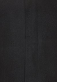 Černý vlněný kabát s hladkou texturou, na míru střižený a svislými švy. Má čistý, minimalistický design bez vnějšího kovového vybavení.