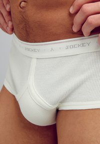 Slip in cotone bianco a costine con un morbido elastico in vita caratterizzato da testo ripetuto "Jockey". Inquadratura ravvicinata che si concentra sulla texture e sulla vestibilità.