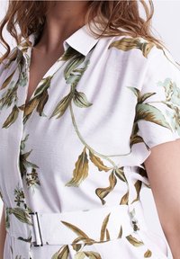 Abito camicia bianco a maniche corte con stampa botanica verde e marrone, colletto e cintura coordinata con fibbia argentata.