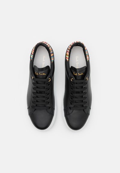 Black leather sneakers with a white sole, featuring gold eyelets, flat black laces, and a multicolored striped trim around the collar.