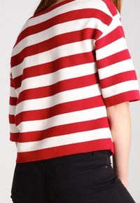 Rot-weißer gestreifter Strickoberteil mit kurzen Ärmeln, lockerer Passform und geripptem Ausschnitt. Kombiniert mit figurbetonten schwarzen Hosen.