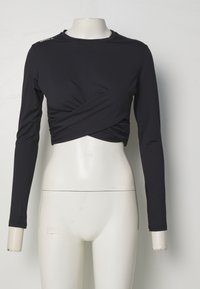 Crni dugi rukav uski crop top s drapiranim prednjim dijelom i glatkom, laganom tkaninom. Sadrži suptilan detalj s logotipom na ramenu.