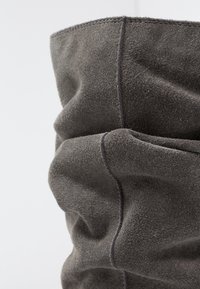 Stivale grigio in suede con una texture morbida, caratterizzato da pieghe arricciate e cuciture a contrasto lungo le cuciture. Il bordo superiore è leggermente arrotolato.