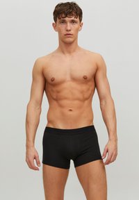 Schwarze Boxershorts mit tailliertem Design. Weicher Stoff, elastischer Bund mit Logo. Modell hat einen durchtrainierten Körper, Arme entspannt an den Seiten.