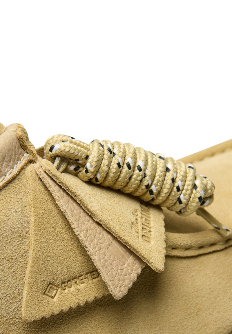 Yellow suede shoe with a textured surface, featuring an intricately knotted golden rope accent and leather tags embossed with GORE-TEX.