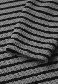 Grau gestrickter Stoff mit strukturierter Oberfläche, der horizontale schwarze Streifen aufweist. Enthält einen umgeschlagenen Saum für zusätzliche Details.