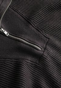 Maglione grigio scuro con un motivo a coste texturizzato. Presenta una chiusura a quattro quinti con zip metallica e colletto alto.