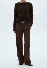 Hnědý pletený svetr s dlouhými rukávy, kombinovaný s hnědými kostkovanými širokými kalhotami a černým opaskem se stříbrnou sponou. Hnědé boty dokončují vzhled.