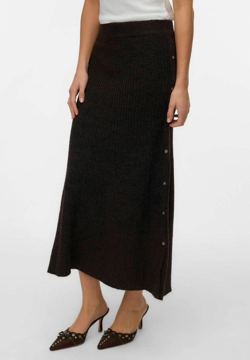 Jupe maxi en maille marron foncé avec une texture côtelée, détail de boutons sur le côté et une taille ajustée, associée à des mules à talons aiguilles.