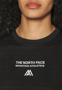 Svart idrottströja med rund halsringning, med vit text: "THE NORTH FACE MOUNTAIN ATHLETICS" och en logotyp. Texturerad tygdesign.