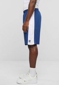 Blå og hvide atletikshorts med elastisk talje, lavet af glat stof. Et logo er synligt nær kanten på den blå side.
