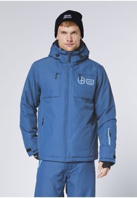 Blaue isolierte Jacke mit Kapuze, zwei Brusttaschen, Frontreißverschluss und schwarzen Akzenten. Glatte Textur mit minimaler Markenkennzeichnung.