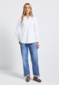 Chemise blanche à manches longues avec patte de boutonnage, associée à un jean bleu clair à ourlet et des ballerines en cuir marron à motif léopard. Design simple et épuré.