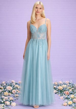 Donna bionda in un abito senza maniche di tulle azzurro chiaro con corpetto in pizzo floreale, in piedi su un pavimento lavanda sparso di fiori.