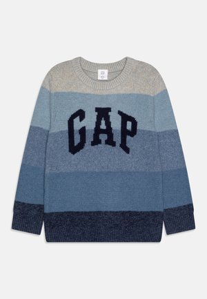 Pull en maille épaisse à rayures horizontales beige et nuances de bleu, avec de grandes lettres noires "GAP" sur la poitrine.
