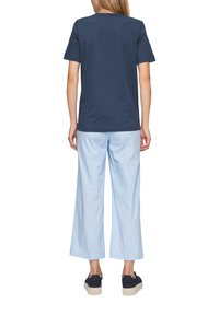 Dunkelblaue Baumwoll-T-Shirt mit kurzen Ärmeln, kombiniert mit hellblauen weiten Hosen. Schwarze Sneaker mit beigen Sohlen.