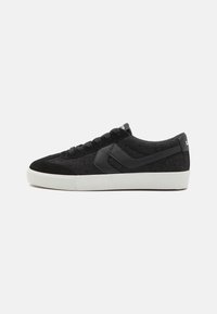 Schwarze Wildleder- und Stoff-Sneaker mit strukturiertem Obermaterial, weißer Gummisohle und Schnürdesign. Mit einem schwarzen Akzentlogo an der Seite.