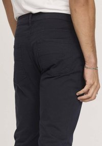 Pantalon bleu foncé au design polyvalent, avec des poches arrière et des coutures discrètes. Le tissu semble doux avec une texture lisse.