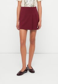 Bordeaux plissée mini-jurk gemaakt van gestructureerde stof, gecombineerd met zwarte lakleren ballerina's met een strikdetail. Eenvoudig, klassiek ontwerp.