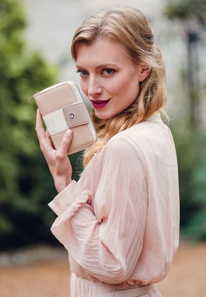 Beige zippered wallet with a light cream accent and round logo. Textured surface with smooth detail and contrasting clasp hardware.