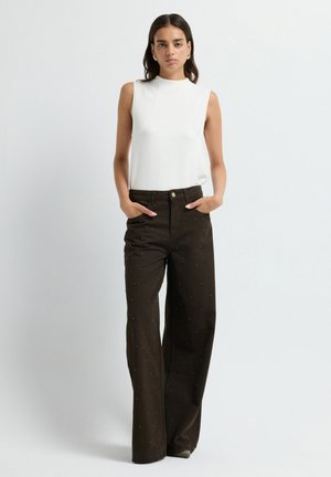 Haut sans manches blanc avec un col montant, accompagné de pantalons larges marron ornés de clous en argent et de poches avant.