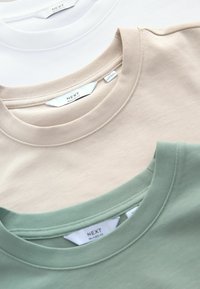 Tre crew-neck T-shirts i hvid, beige og grøn. Lavet af blødt bomuld med ribbede kraver og mærker synlige ved halsudskæringerne.
