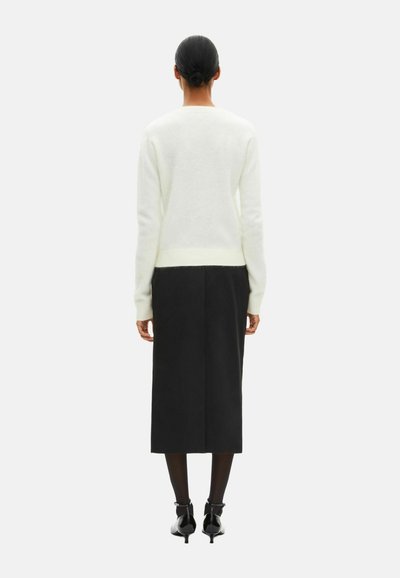 Hvid, let sweater med lange ærmer, kombineret med et sort, knælængde skørt. Outfittet har enkle linjer og en blød tekstur.