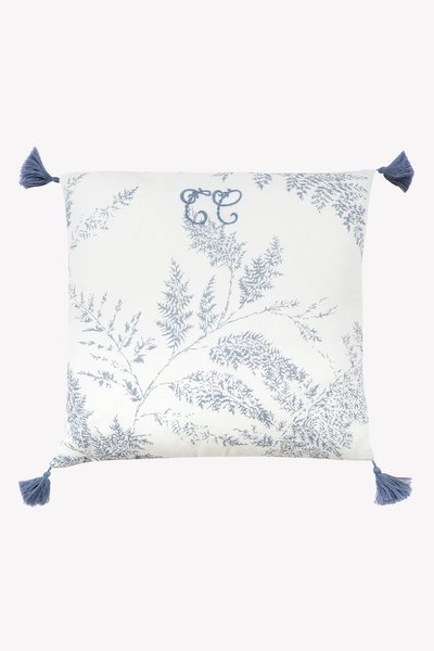 Τετράγωνο διακοσμητικό μαξιλάρι με λευκό φόντο, μπλε μοτίβο φτέρης και μπλε φούντες σε κάθε γωνία. Διαθέτει διακοσμητικό μονόγραμμα 'CC'.