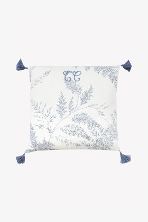 Kvadratinė dekoratyvinė pagalvėlė su balta fone, mėlynu paparčio raštu ir mėlynomis kutomis kiekviename kampe. Turi dekoratyvinį „CC“ monogramą.