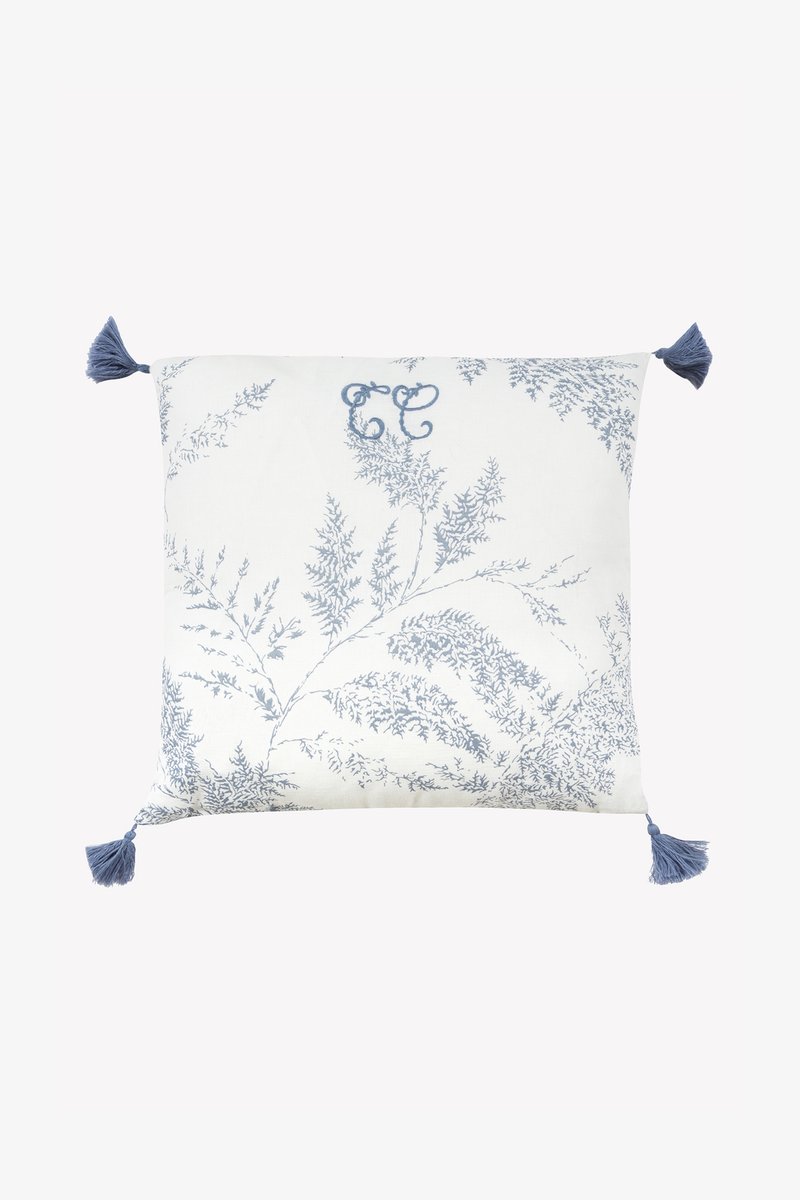 Τετράγωνο διακοσμητικό μαξιλάρι με λευκό φόντο, μπλε μοτίβο φτέρης και μπλε φούντες σε κάθε γωνία. Διαθέτει διακοσμητικό μονόγραμμα 'CC'.