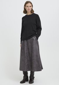 Mustast kooel olev ümar-kaelusega kampsun, mille kõrval on metallik tumehall pikk seelik. Modell kannab musti nahast põlvik-saapaid.