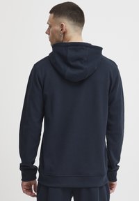 Felpa con cappuccio di colore blu navy in un tessuto testurizzato, caratterizzata da maniche lunghe e una vestibilità rilassata. Il cappuccio e i polsini a costine offrono ulteriore comfort.