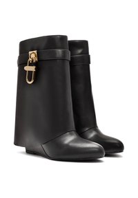 Bottes de cheville en cuir noir au design épuré, à bout pointu et avec un accent en métal doré, incluant une boucle décorative sur le dessus.