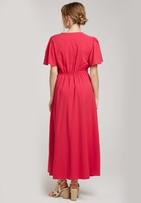 Robe maxi en rose vif, fabriquée à partir d'un tissu lisse. Elle possède des manches courtes et légères ainsi qu'une taille élastique, avec une jupe fluide.