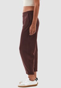 Bordeaux joggings met zijzakken en geborduurde broekspijpen, gemaakt van zachte stof, gecombineerd met witte en grijze sneakers.