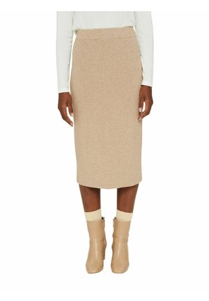 Jupe midi beige en maille avec une silhouette ajustée. Elle présente une taille haute et un ourlet arrivant à mi-longueur, associée à des bottines neutres.