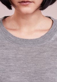 Szary dziany sweter z okrągłym dekoltem. Gładka faktura, dopasowany fason i ściągacz przy dekolcie. Prosty, jednolity kolor bez wzorów.