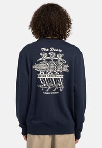 Sudadera de color navy con un gráfico en la parte trasera de tres esqueletos sosteniendo un tronco, con el texto "Los Hacedores" y "CONSTRUIR ALGO", puños y dobladillo acanalados.