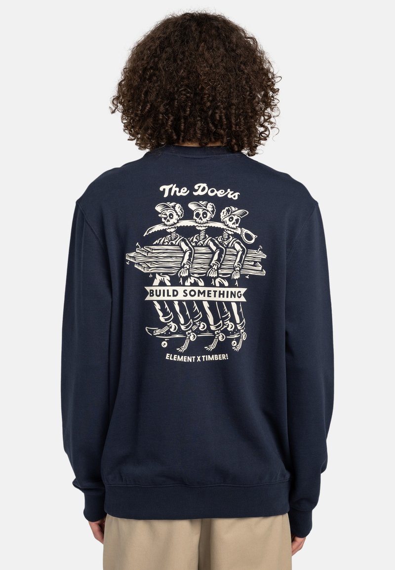 Sudadera de color navy con un gráfico en la parte trasera de tres esqueletos sosteniendo un tronco, con el texto "Los Hacedores" y "CONSTRUIR ALGO", puños y dobladillo acanalados.