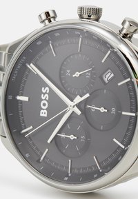 Montre chronographe en argent avec un cadran gris foncé, dotée de trois sous-cadrans, de repères blancs, d'un affichage de la date et d'accents en métal poli.