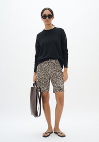 Pull noir à manches longues, short beige à imprimé léopard, tongs noires et sac fourre-tout marron. Textures lisses, design décontracté.