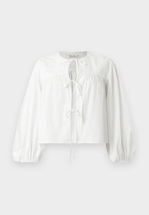 Blouse blanche à manches longues avec un empiècement froncé, un col rond et trois liens à l’avant, présentée sur un fond clair uni.