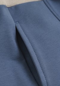 Blaues Strickgewebe mit einer strukturierten Oberfläche, das einen vertikalen Schlitz und saubere Nähte entlang der Kante aufweist, was ein geschichtetes Aussehen verleiht.