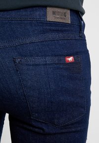 Mörkblåa jeans i denim med en signaturläderlapp med texten "MUSTANG" på midjebandet och en liten röd etikett på bakfickan.