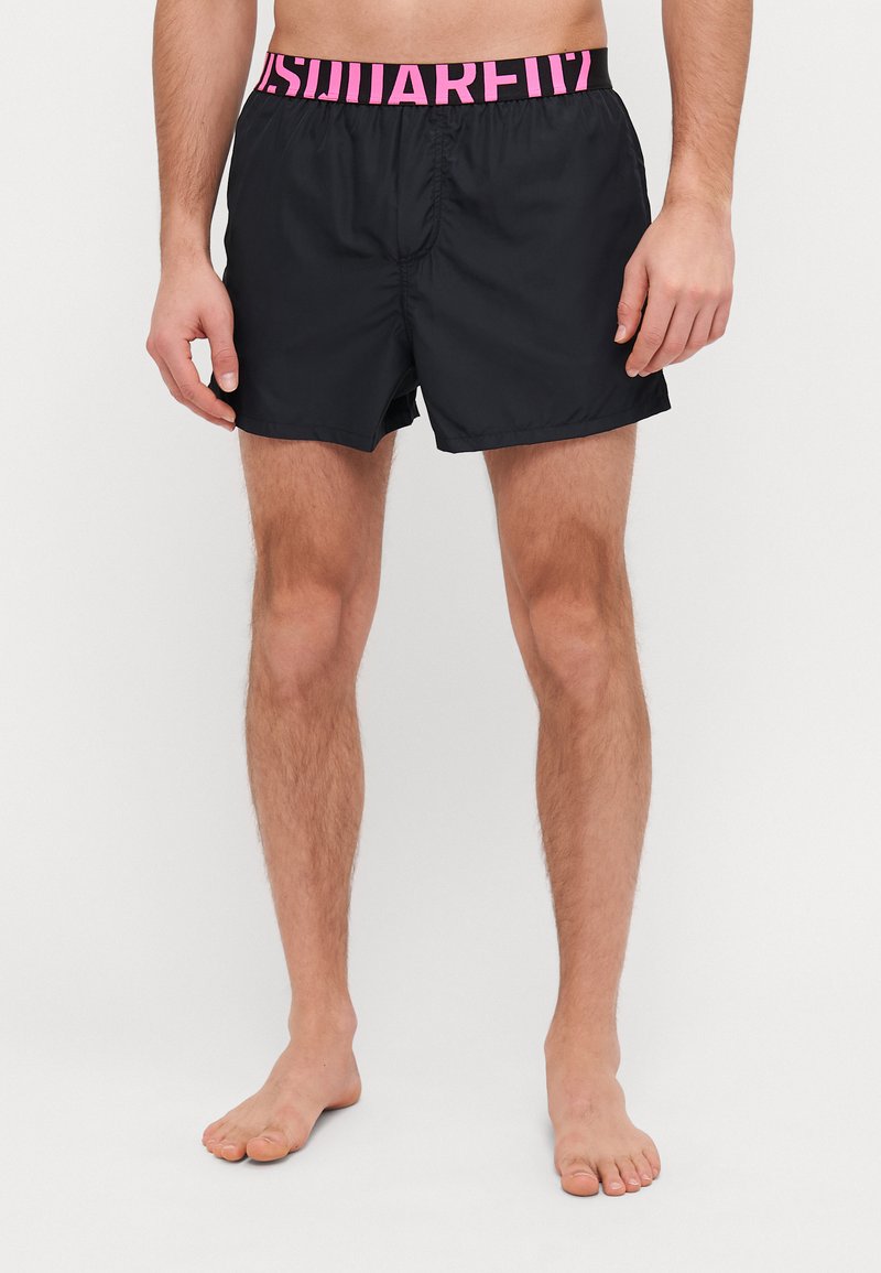 Schwarze Badeshorts mit einem rosa elastischen Bund, auf dem der Text "SQUARE" steht. Die Shorts haben ein einfaches Design und eine glatte Textur.