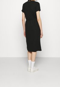 Svart klänning med kort ärm och avslappnad passform, knälång, med en samlad midja. Matchad med vita ankelsockor och sneakers.