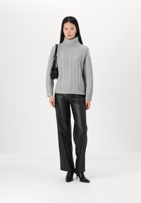 Pull en maille torsadée gris, léger, associé à un pantalon en cuir noir taille haute et des bottines à talons. Détail de sac à main noir.