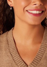 Silver hoop earrings with a small, clear gemstone pendant, worn with a light brown, textured v-neck sweater.