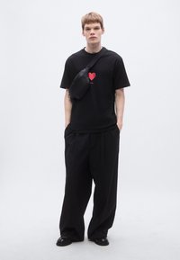 Μαύρο μπλουζάκι με κόκκινη καρδιά, συνδυασμένο με άνετο μαύρο παντελόνι και μαύρη τσάντα χιαστί. Λείο ύφασμα και χαλαρή εφαρμογή.